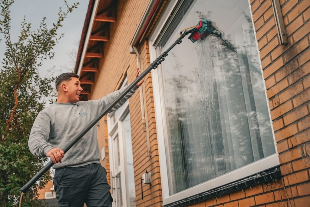 Professional window cleaner working with a long pole outside a house